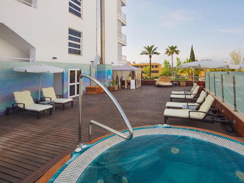 Area piscina moderna su terrazza in legno con lettini e vasca idromassaggio in un hotel.