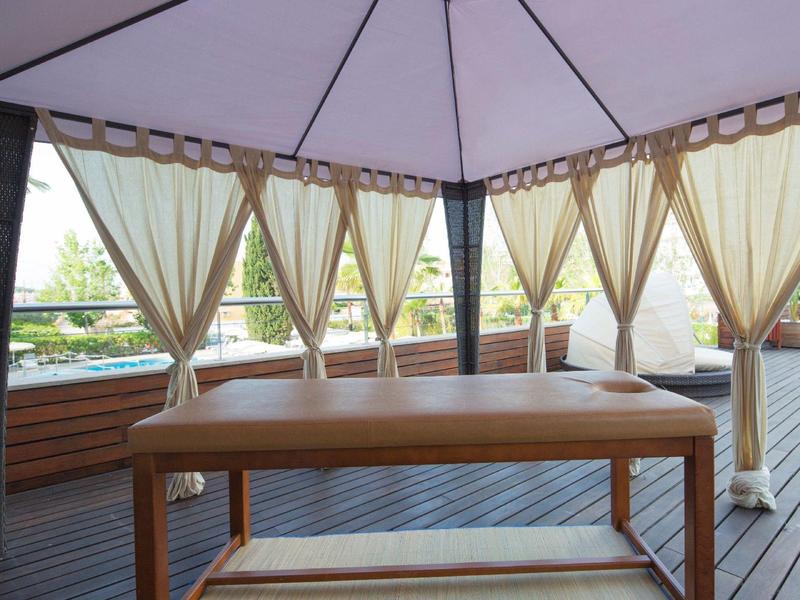 Lettino da massaggio sotto una tenda con tende trasparenti su un terrazzo in legno.