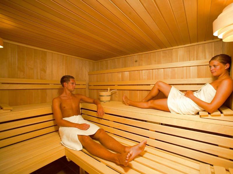 Due persone si rilassano in una sauna di legno, entrambe avvolte in asciugamani bianchi.