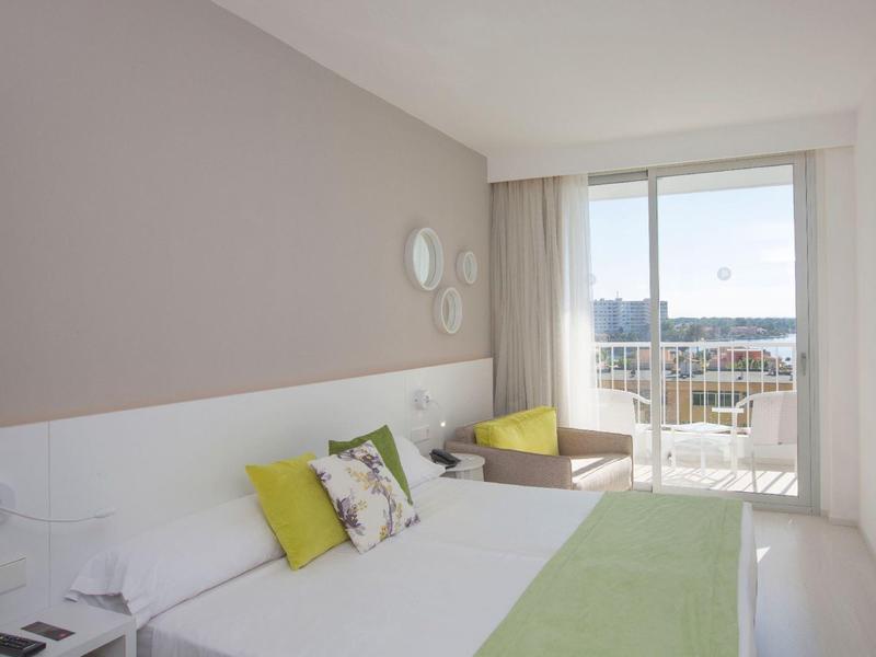 Camera d'hotel moderna con letto matrimoniale, balcone e vista sulla città alla luce del giorno.