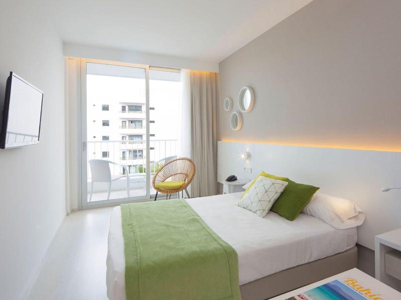 Camera moderna con letto matrimoniale, runner verde, sedia e balcone con vista sulla città.