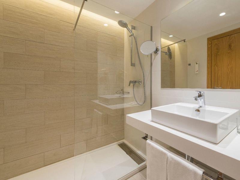 Bagno di hotel moderno con doccia a pavimento, lavabo bianco e accenti in legno.