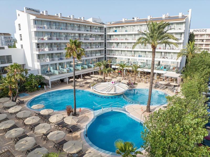 Hotel con due piscine, ombrelloni e palme in un'area esterna soleggiata.