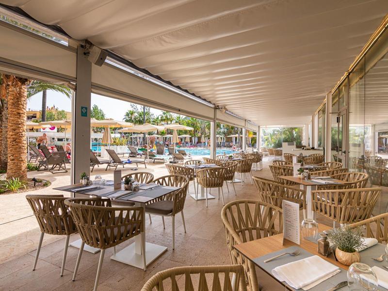 Terrazza coperta con tavoli e sedie che si affaccia su una piscina in un resort.
