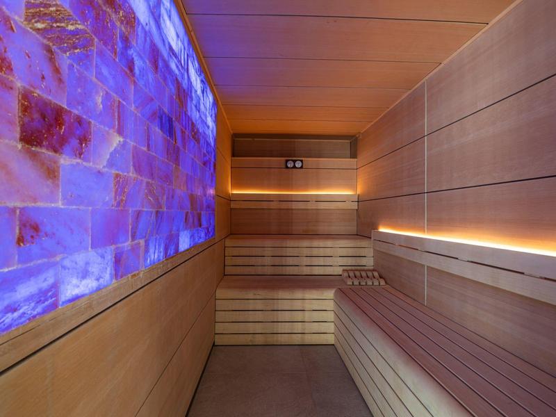 Sala sauna con pannelli in legno, panchine e parete illuminata di blu