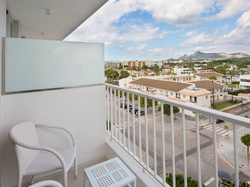 Balcone con sedia bianca e piccolo tavolo, vista su case residenziali e montagne alla luce del giorno.