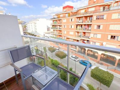 Balkon s dvěma židlemi a skleněným stolem s výhledem na obytné budovy pod jasnou oblohou.