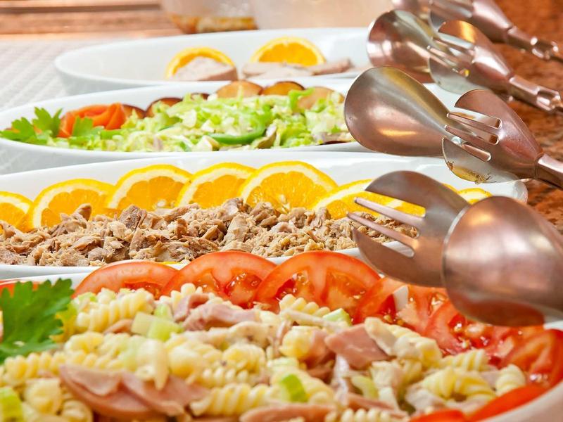 Buffet avec différentes salades, tranches de tomate et tranches d'orange sur une table en bois