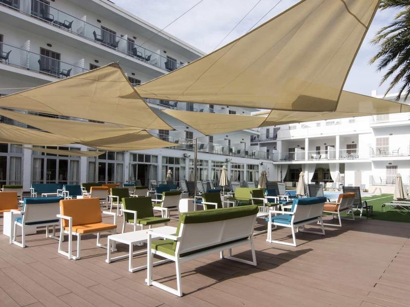 Espace extérieur moderne d'un hôtel avec des bancs colorés et de grandes toiles d'ombrage.