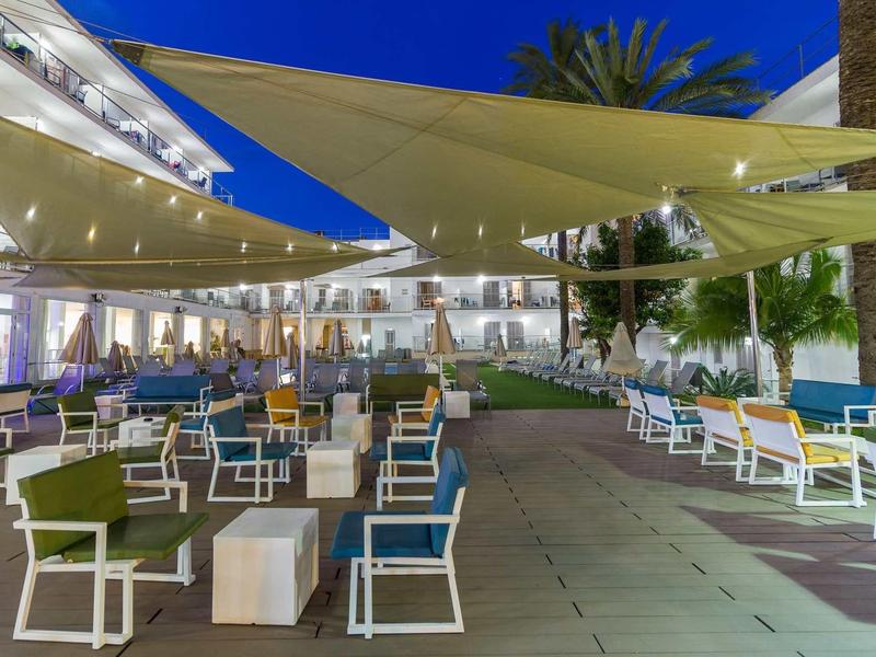 Espace extérieur moderne d'un hôtel avec des chaises colorées et des toiles d'ombrage la nuit.