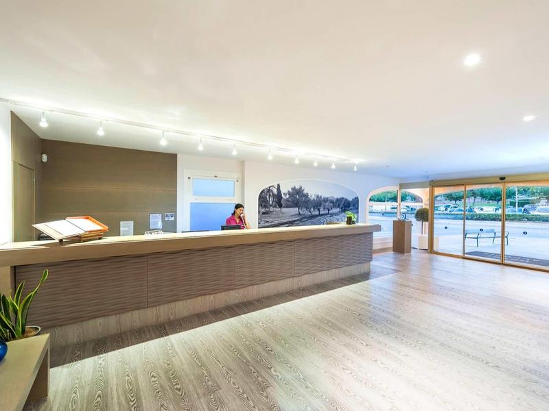 Hall d'hôtel lumineux avec un long comptoir d'accueil et de grandes fenêtres donnant sur l'extérieur.