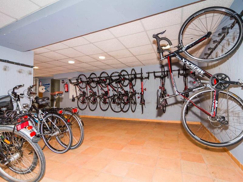 Salle de stockage de vélos avec des vélos suspendus verticalement au mur et plusieurs vélos garés.