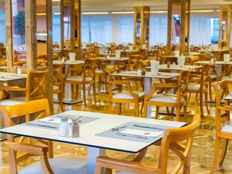 Salle à manger lumineuse avec de nombreuses chaises en bois et des tables blanches.