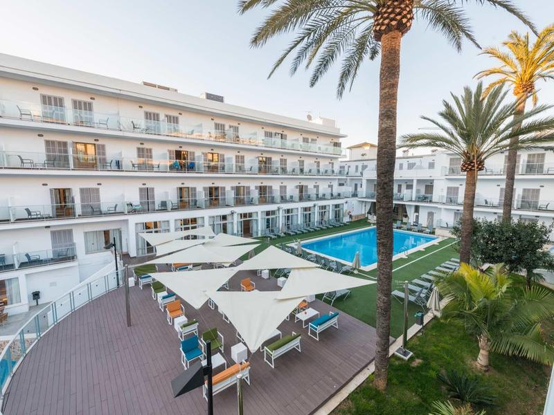 Hôtel moderne avec piscine extérieure, parasols et palmiers sur la terrasse.