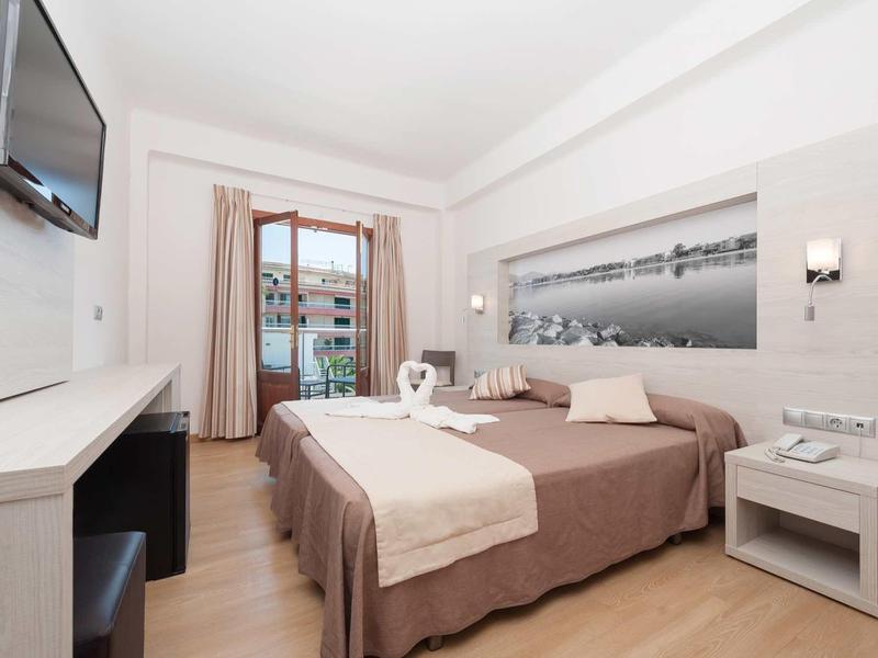 Chambre double lumineuse avec balcon, TV et mobilier moderne en bois clair.