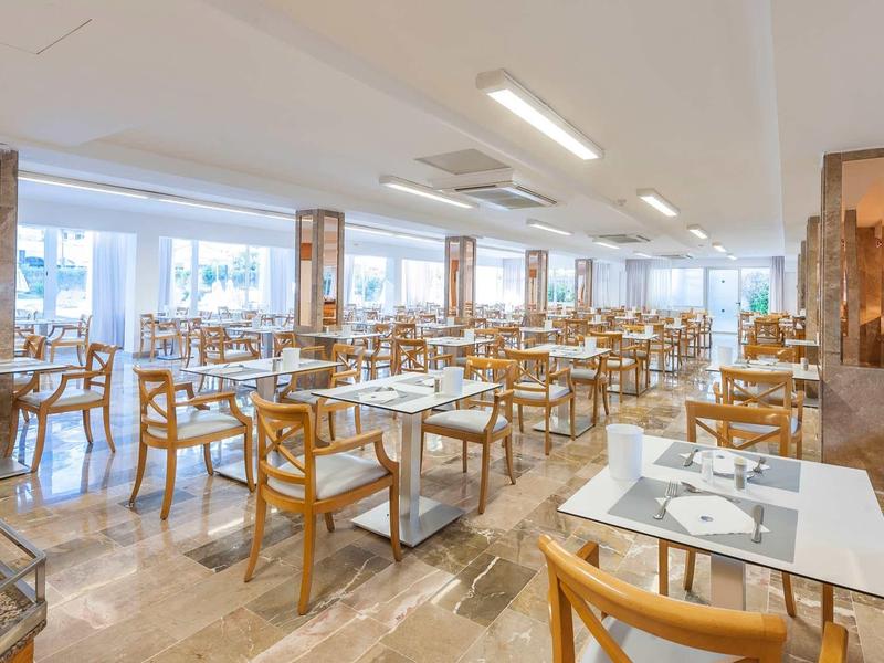 Grande salle à manger lumineuse avec mobilier en bois et plateaux blancs dans un hôtel.