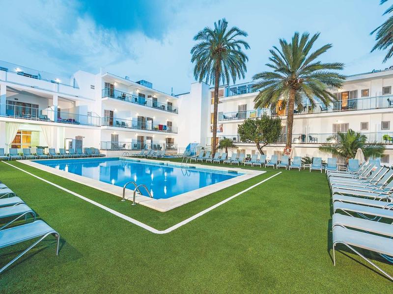 Espace piscine d'hôtel moderne avec chaises longues et palmiers sur pelouse verte sous ciel nuageux