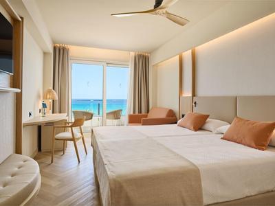 Lichte hotelkamer met twee bedden, zithoek en zeezicht door grote ramen.