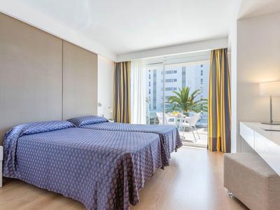 Lichte hotelkamer met twee eenpersoonsbedden, groot raam en toegang tot terras met tuinmeubilair.