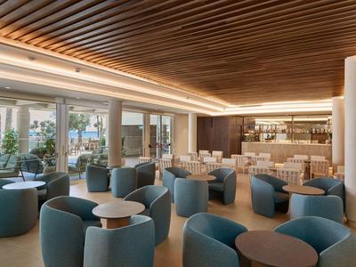 Moderne hotel-lounge met blauwe stoelen, houten lattenplafond en natuurlijk licht.
