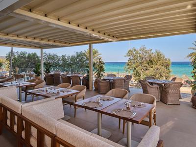 Overdekt terras met tafels, stoelen en uitzicht op zee en bomen.