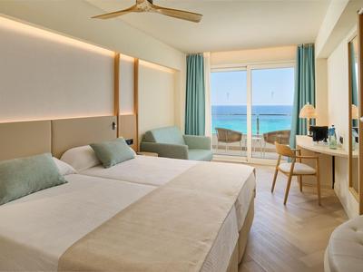 Licht hotelkamer met twee eenpersoonsbedden, balkon en uitzicht op zee.