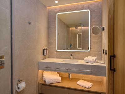 Moderne badkamer met verlichte spiegel, wastafel, handdoeken en lichte houtaccenten.