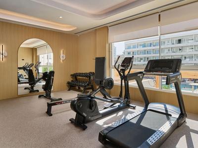 Salle de sport moderne avec tapis de course, rameur et vue sur la ville.