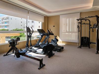 Salle de sport moderne avec divers équipements d'exercice et grandes fenêtres donnant sur des bâtiments environnants.