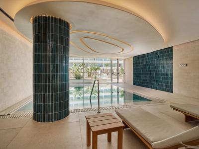 Piscine intérieure moderne avec colonne, transats et baie vitrée donnant sur l'extérieur dans un hôtel.