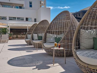 Fauteuils lounge modernes en forme d'œuf avec coussins verts sur une terrasse d'hôtel ensoleillée.