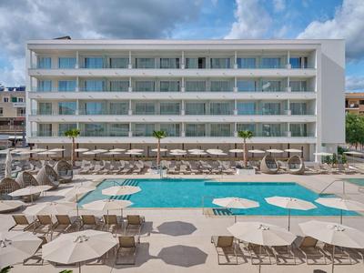 Hôtel moderne avec piscine, chaises longues et parasols sous un ciel nuageux.