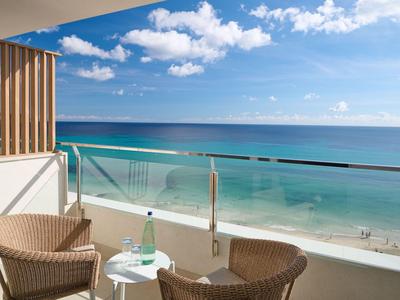 Balcon avec deux fauteuils et une petite table surplombant la mer et la plage de sable sous un ciel bleu.