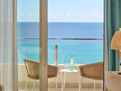 Balcon avec deux chaises et une table donnant sur la mer bleue sous un ciel clair.