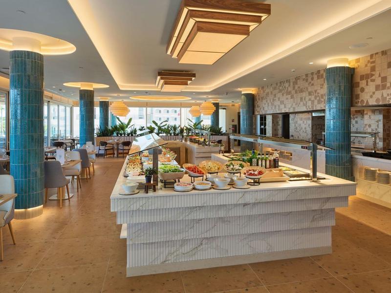 Lichte, moderne ontbijtzaal met buffet en zitgedeeltes in een hotel.