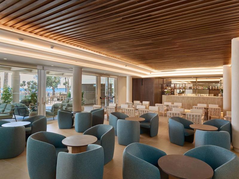Moderne hotel-lounge met blauwe stoelen, houten lattenplafond en natuurlijk licht.