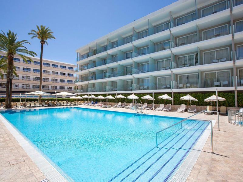 Modern hotelzwembad met ligstoelen en parasols onder een heldere blauwe lucht.