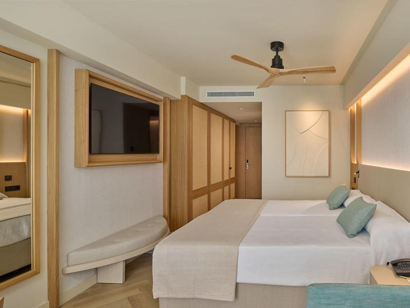 Modern hotelkamer met tweepersoonsbed, houten kasten en plafondventilator.