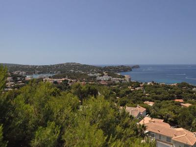 Vista panorámica de un litoral con casas, vegetación y un mar bajo un cielo despejado.