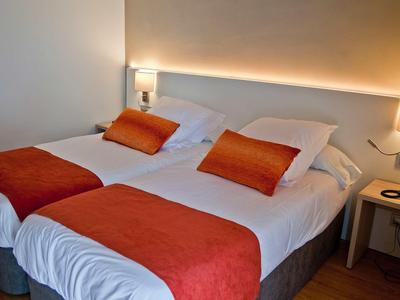 Dos camas individuales con sábanas blancas y mantas y almohadas naranjas en una habitación de hotel.