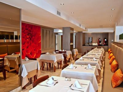 Área elegante de restaurante de hotel con manteles blancos, cojines naranjas y iluminación moderna.