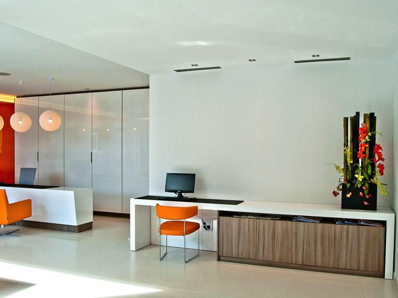 Área de recepción moderna con mostrador blanco, sillas naranjas y decoración minimalista.