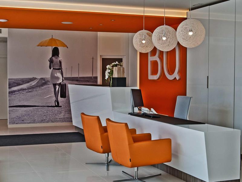 Área de lounge moderno de hotel con sillas naranjas y mostrador de recepción blanco.