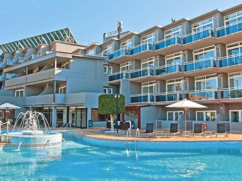 Edificio de hotel con varios balcones y una piscina con fuente en primer plano.