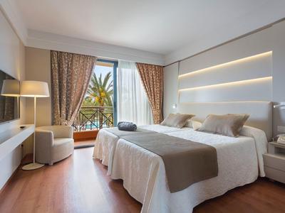 Camera d'hotel moderna con letto matrimoniale, TV a schermo piatto e balcone con vista sulle piante.