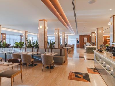 Heldere hotel-lounge met zitgroepen, houten pilaren en receptiebalie.