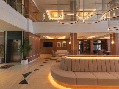 Moderne hotellobby met loungezitplaatsen, planten en liften in warme bruine tinten.