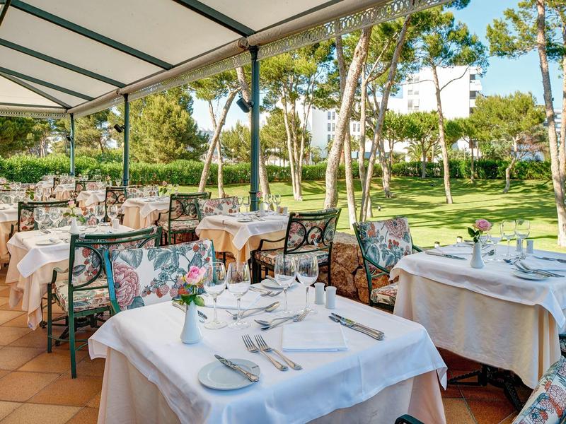 Terrazza del ristorante dell'hotel con tavoli elegantemente apparecchiati e vista sul giardino verde.