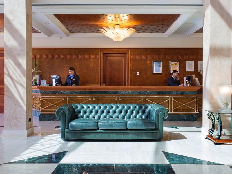 Elegante hall d'hotel con divano in pelle verde e banco in legno sullo sfondo.