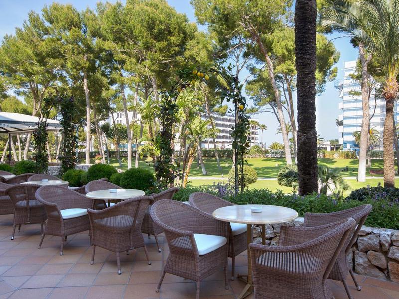 Terrazza dell'hotel con tavoli e sedie in rattan sotto alberi tropicali.